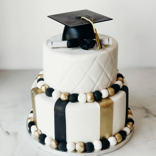 Two-tier graduation cake in black and gold fondant with a diploma and cap topper