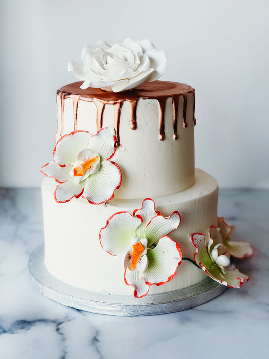 Two-tier cake decorated with florals and a gold drip finish