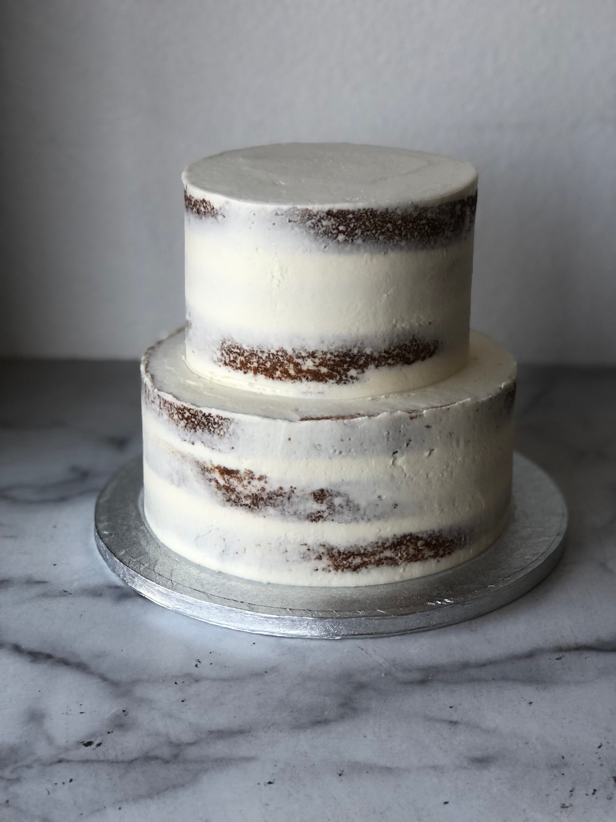 Two-tier semi-naked wedding cake with light buttercream and exposed cake layers