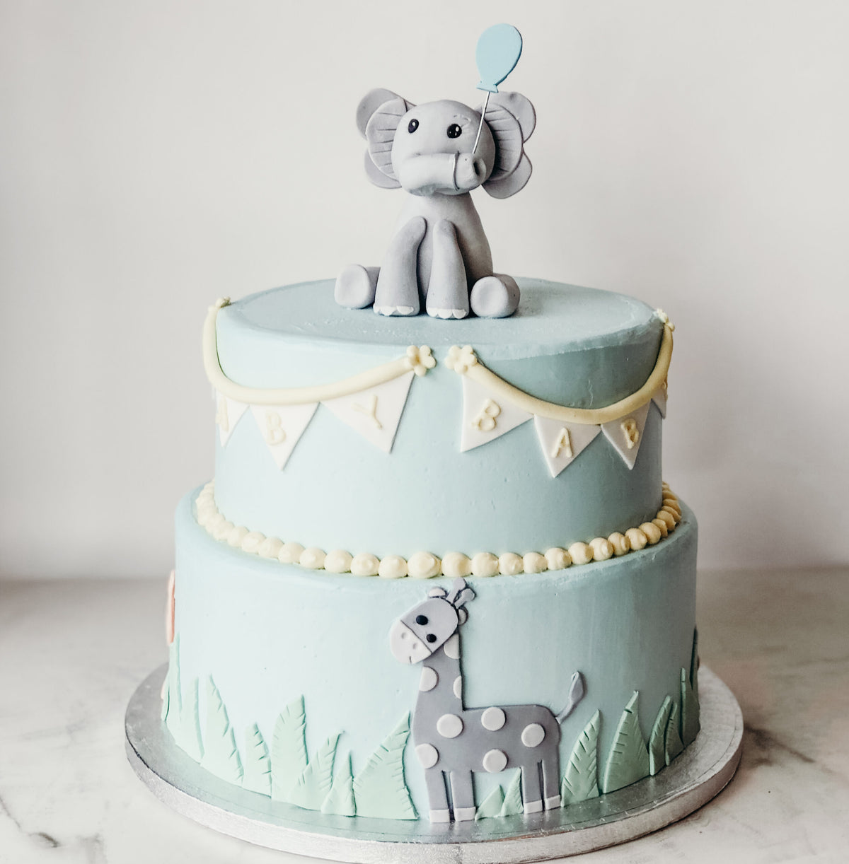 Baby shower cake decorated with safari animals including an elephant and giraffe