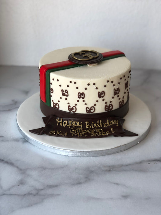 Custom cake decorated with a fondant Gucci-inspired logo and ribbon design