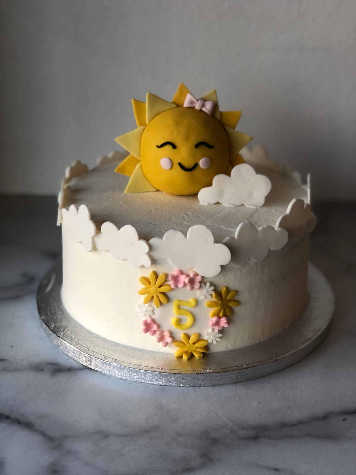 Birthday cake decorated with a cheerful fondant sun, clouds, and pastel flowers