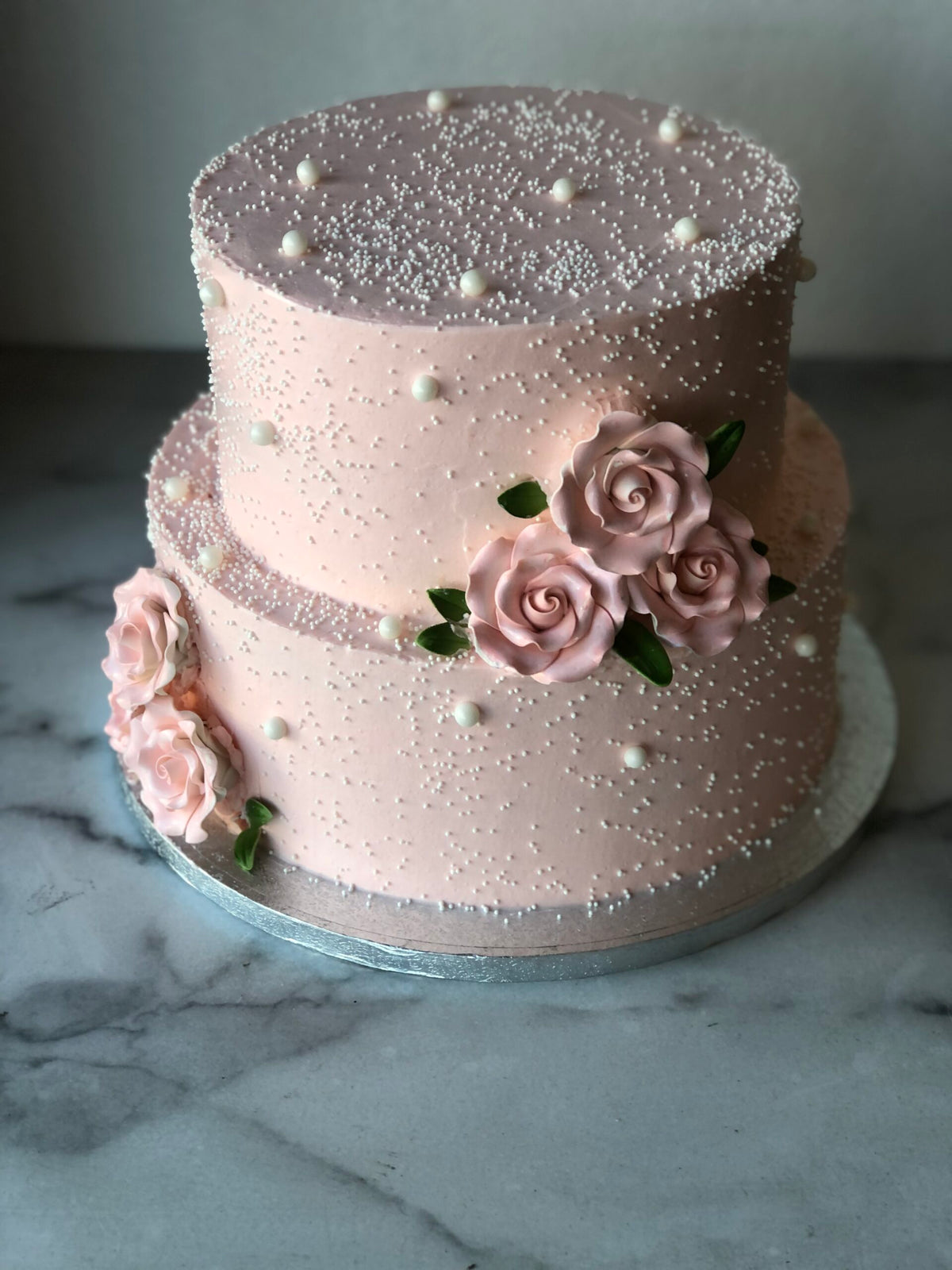 Two-tier wedding cake decorated with pink sugar pearls and delicate roses