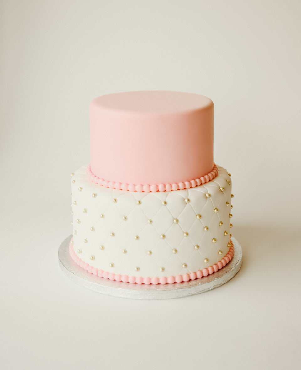 Two-tier birthday cake in pink and white with a soft, classic finish